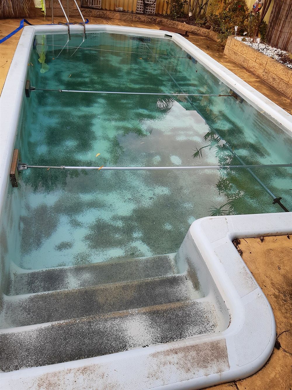 Piscina de fibra com água esverdeada e sem transparência, com manchas no fundo