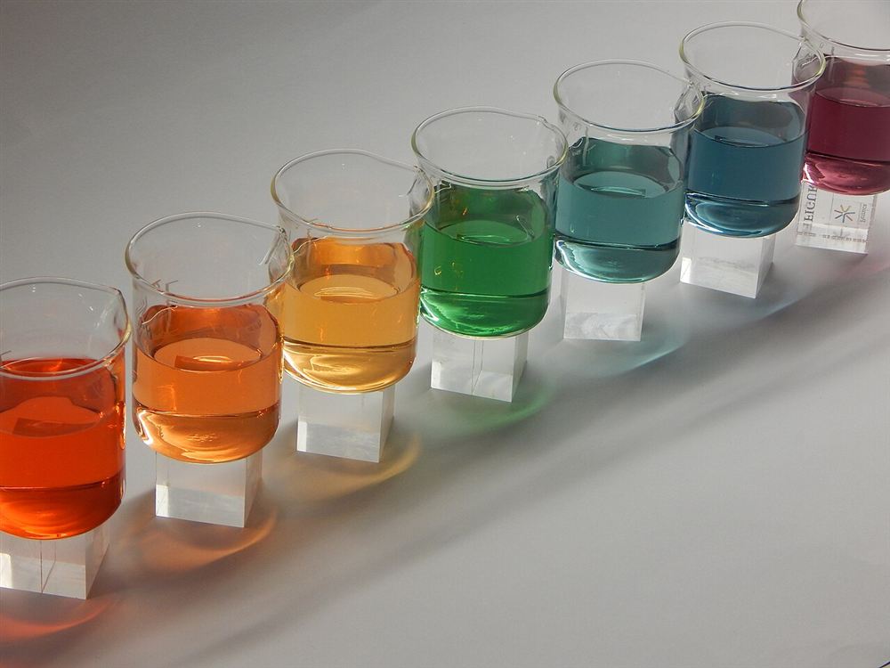 Fileira de copos com soluções de cores do vermelho ao azul, numa escala de indicador