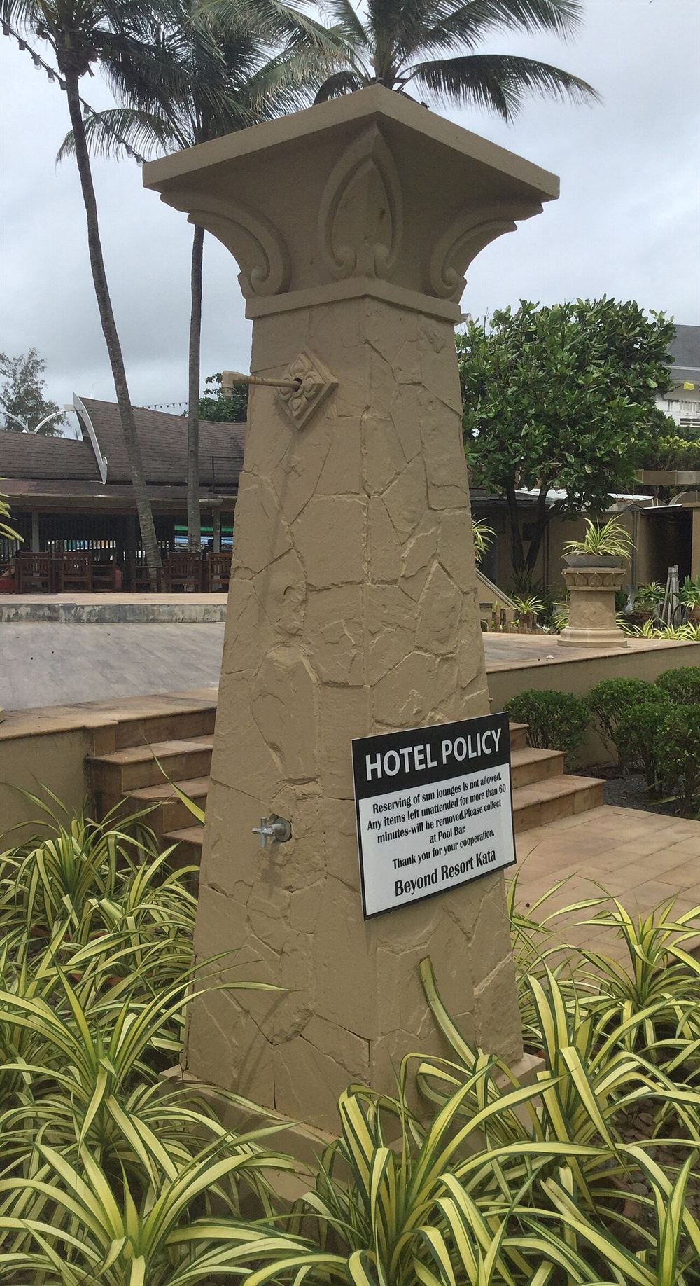 Chuveiro externo em coluna de pedra junto à área de uma piscina de hotel