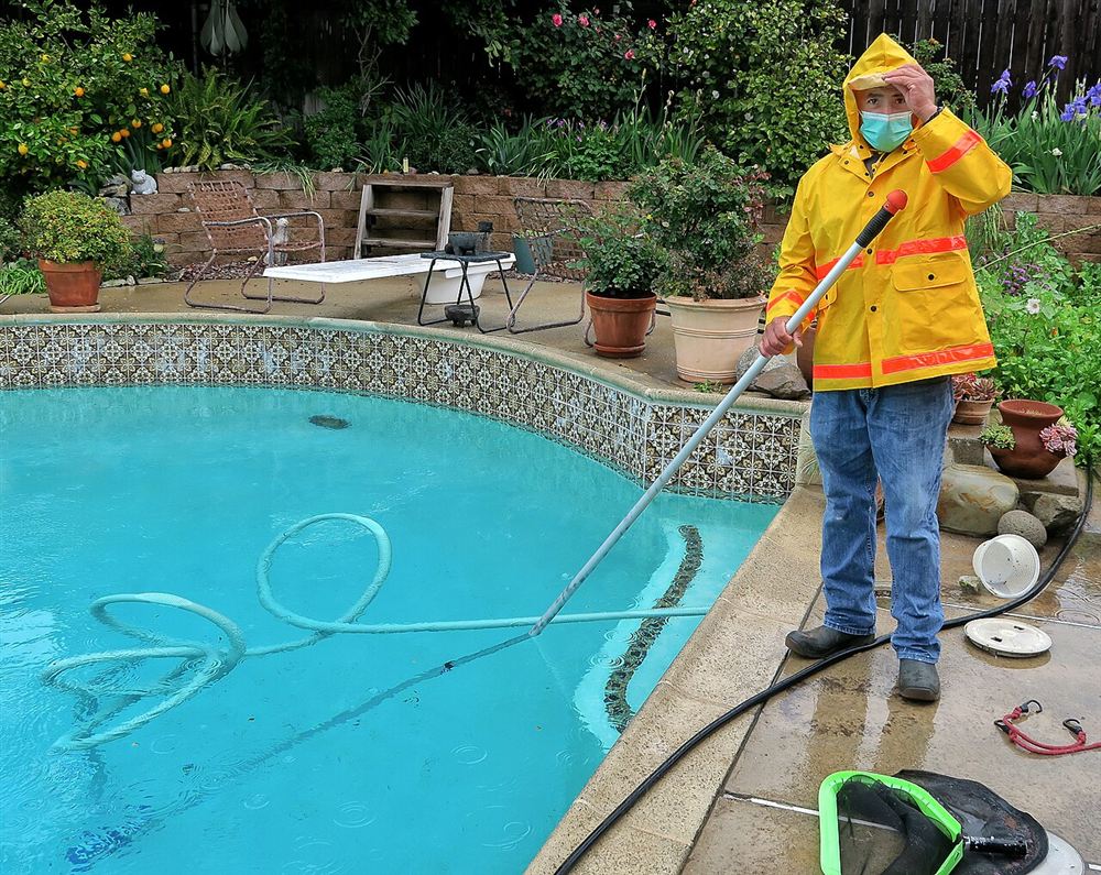 Técnico de capa de chuva aspirando o fundo de uma piscina com o cabo e a mangueira do aspirador