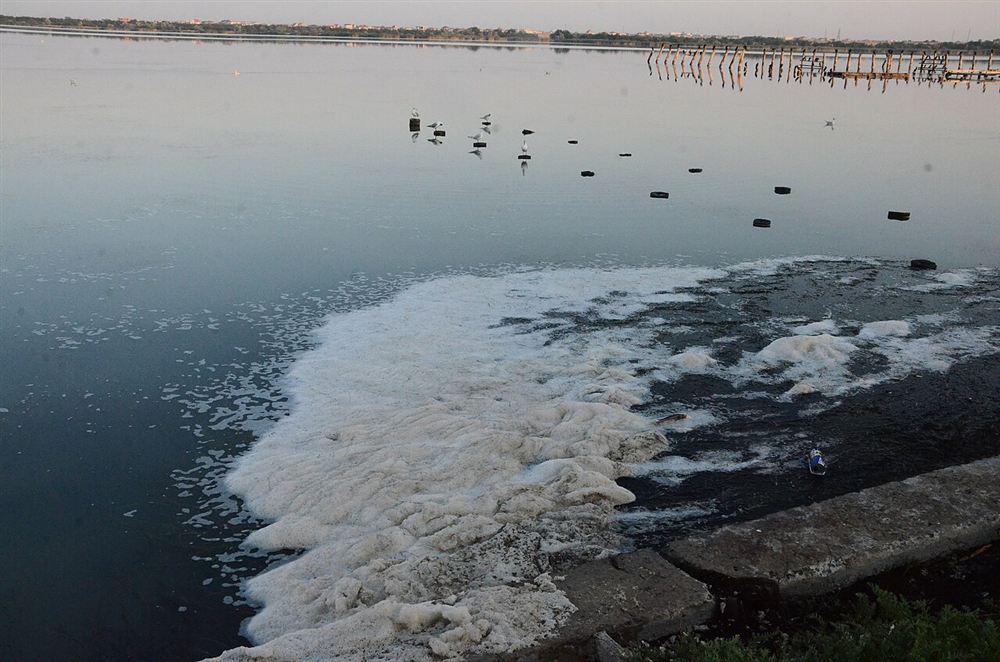 Faixa de espuma branca acumulada na superfície de um lago ao entardecer