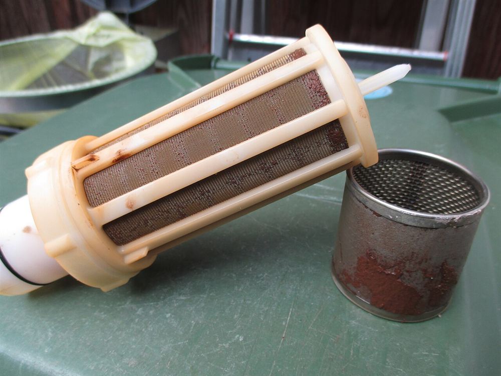 Cartucho de filtro com tela, ao lado do copo do filtro cheio de sujeira acumulada