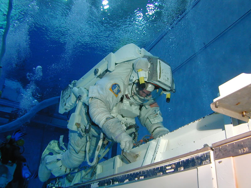 Astronauta com traje espacial completo trabalhando em uma réplica de equipamento da estação espacial, debaixo d'água