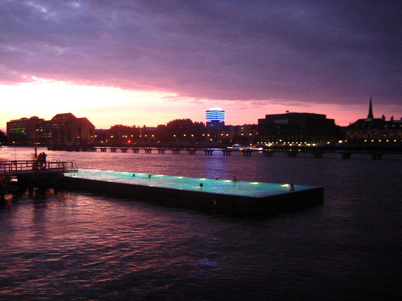 O Badeschiff ao entardecer, uma piscina retangular iluminada flutuando no rio Spree, em Berlim