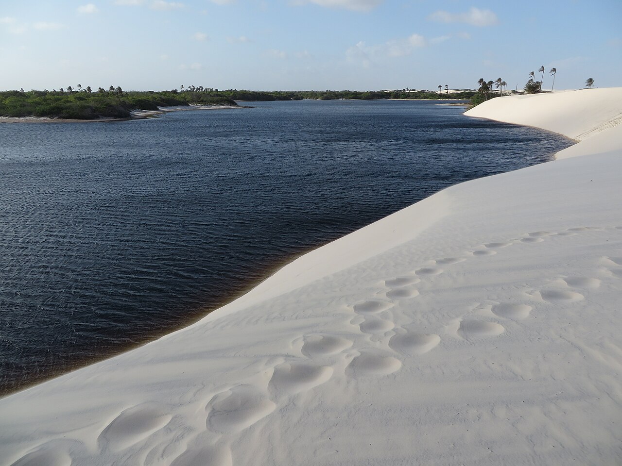 Lagoa de água escura e transparente ao lado de uma duna de areia branca nos Lençóis Maranhenses