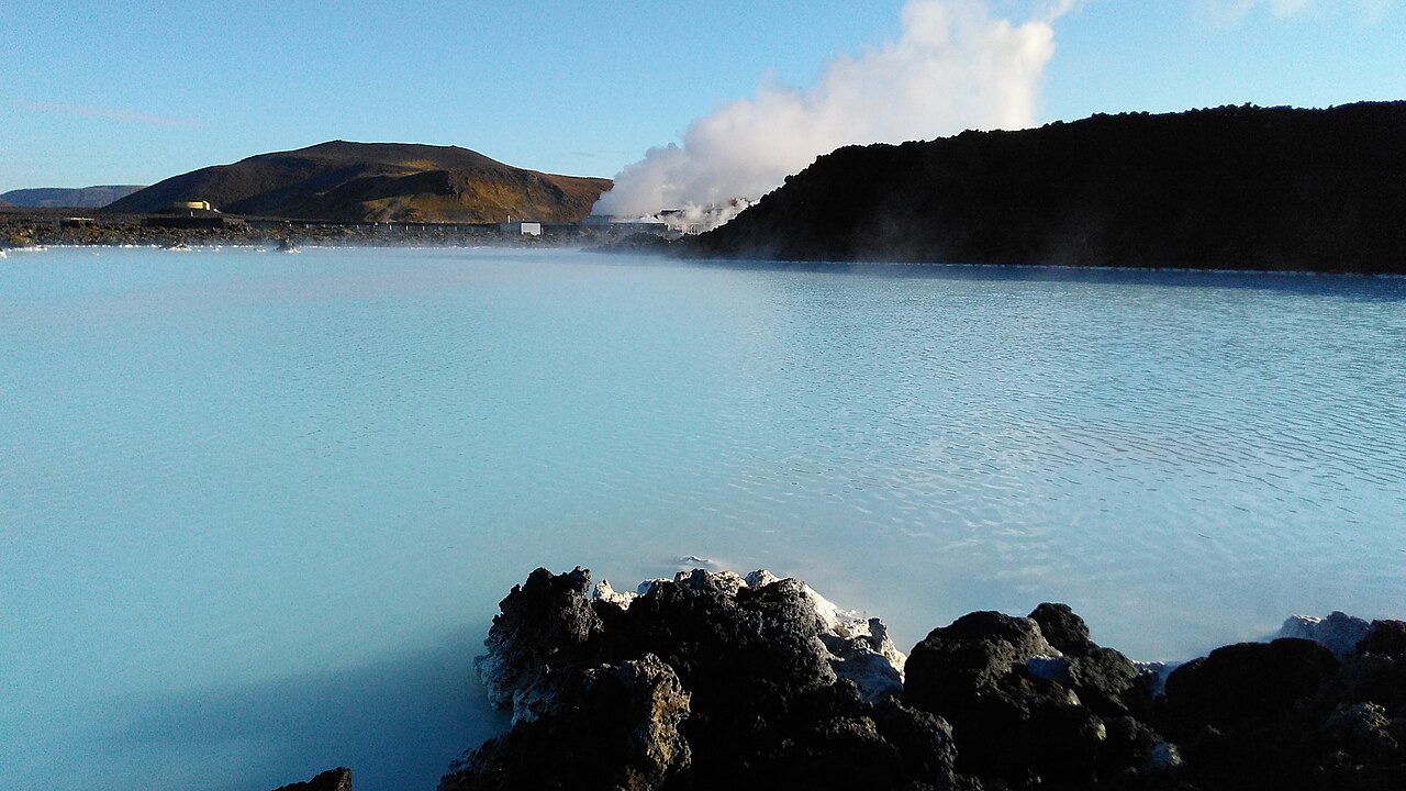 A Blue Lagoon, com água azul-leitosa, rochas de lava em primeiro plano e o vapor da usina geotérmica ao fundo