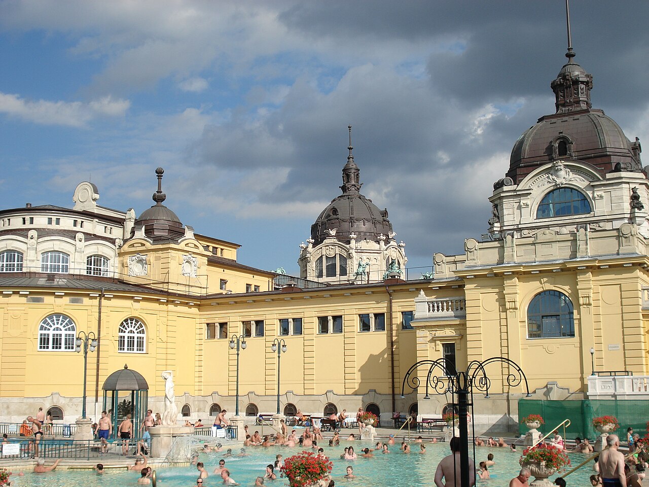 Piscina externa do banho termal Széchenyi, em Budapeste, com o prédio amarelo de cúpulas ao fundo
