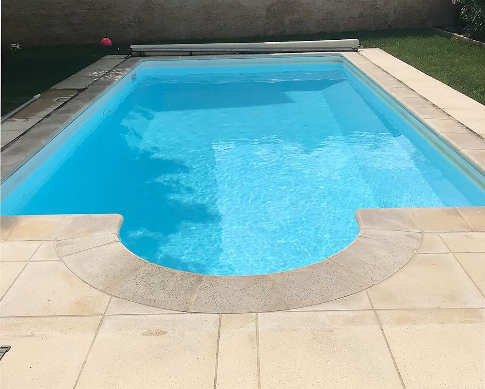 Piscina com borda e deck de pedra clara, de superfície fosca
