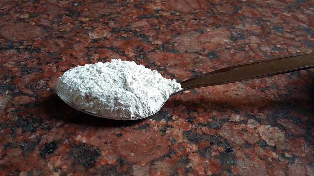 Colher cheia de pó branco de hipoclorito de cálcio sobre um balcão de granito