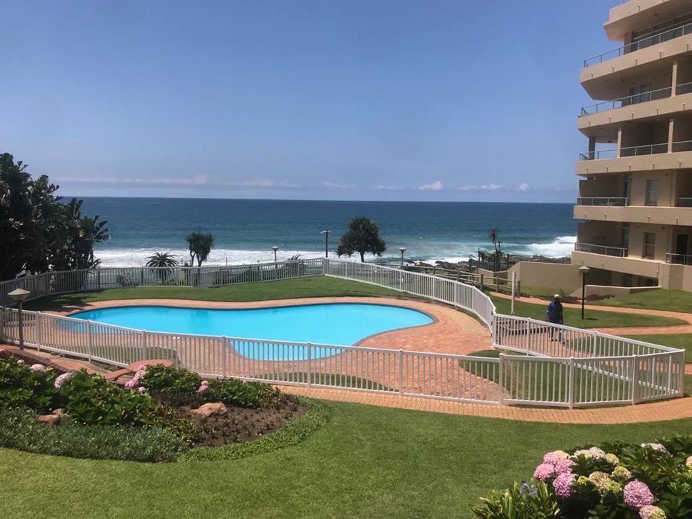 Piscina de condomínio cercada por grade branca com portão, de frente para o mar