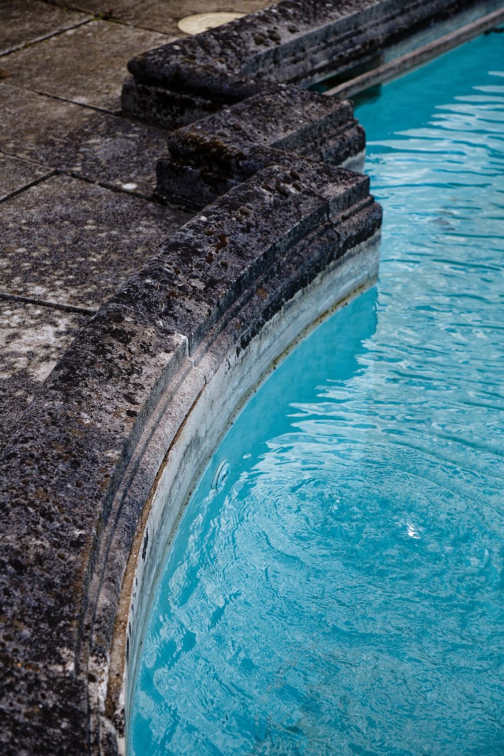 Borda de pedra de uma piscina com a marca do nível da água na parede
